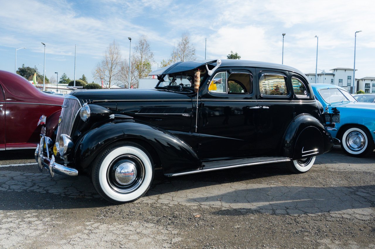 Black prewar classic car with whitewall tires at an outdoor vintage car display.