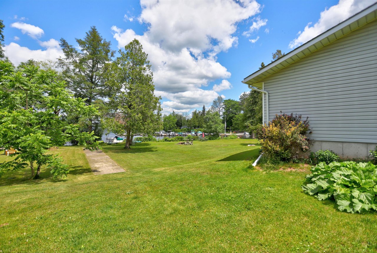 House beside a broad lawn leading to docks and boats, with mature trees along the waterfront.