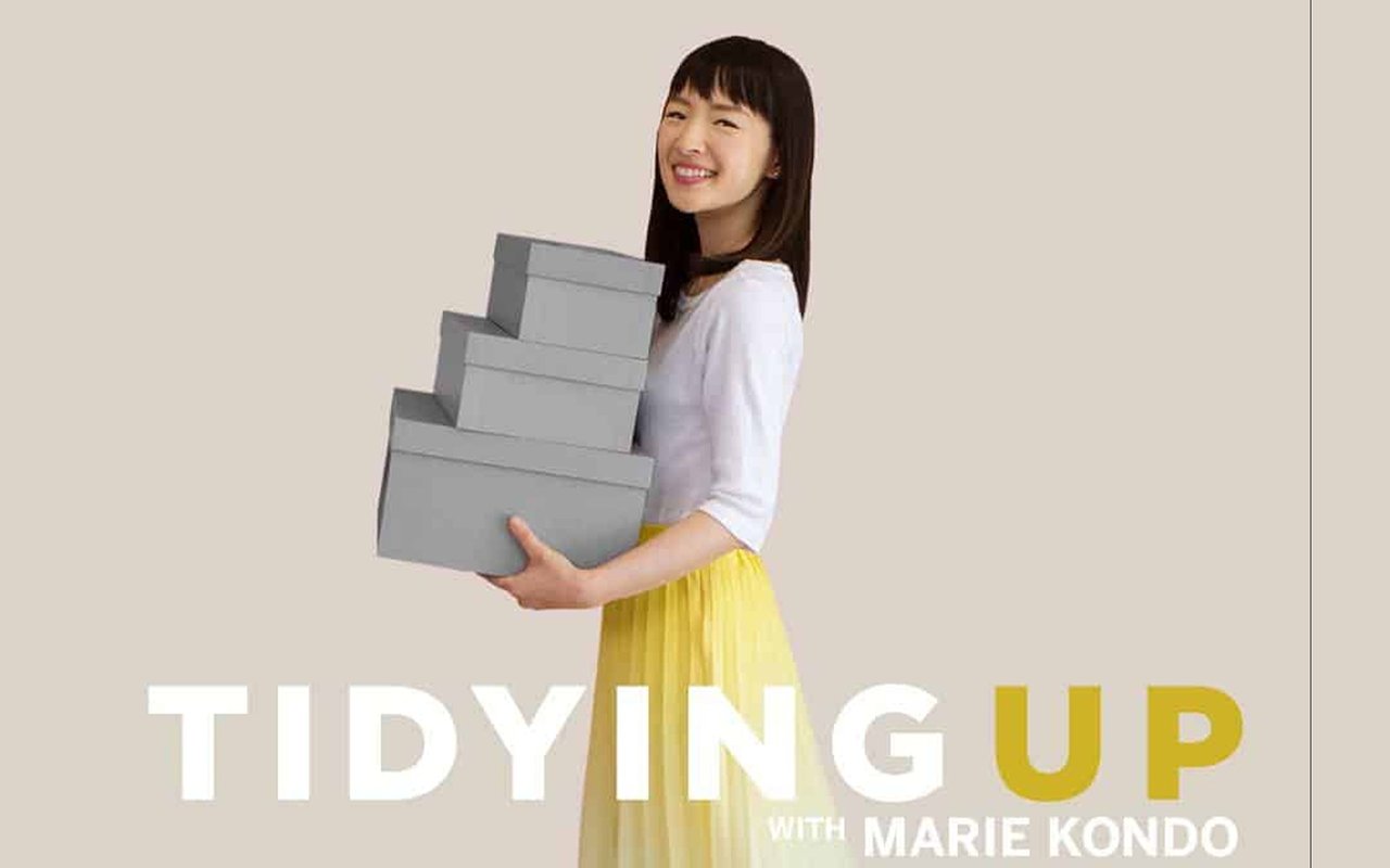 Marie Kondo holds stacked gray storage boxes above the title Tidy­ing Up with Marie Kondo.