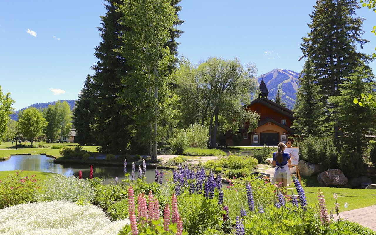 Sun Valley garden with a pond, flower beds, evergreens, and a mountain in the background.