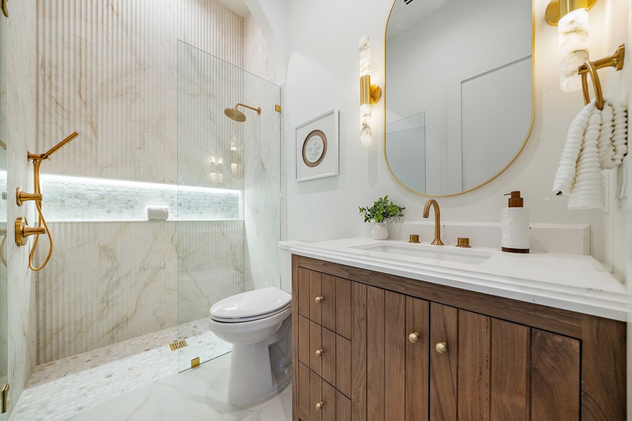Luxury bathroom with a marble-look walk-in shower, gold fixtures, and a wood-front vanity.