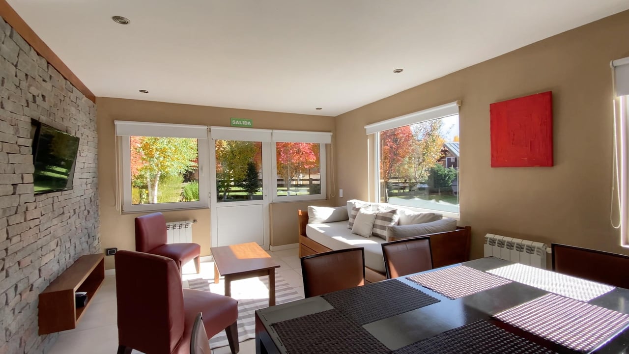 Living and dining room with a stone accent wall and windows overlooking autumn foliage.