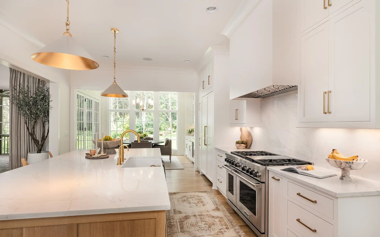 Bright white kitchen with a large marble island, brass fixtures, and a stainless steel range.