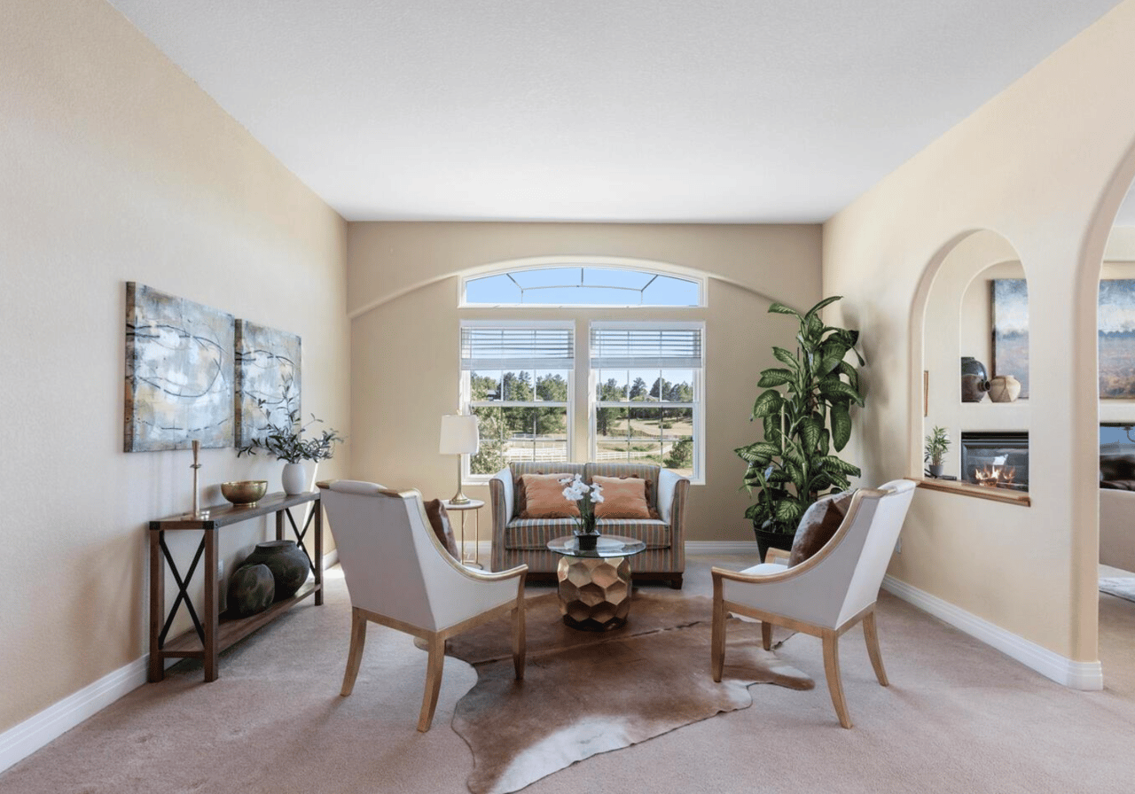 Staged living room with an arched window, seating area, and fireplace visible through an adjoining arch.