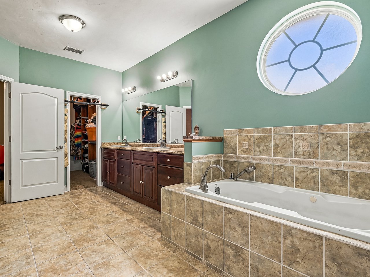 Bathroom with a tiled soaking tub, dark wood double vanity, and large round window.