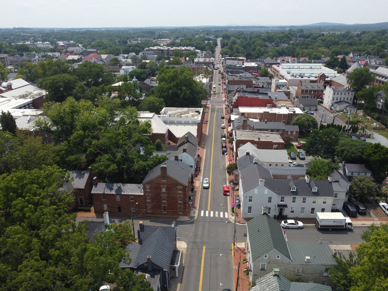 An aerial drone view looking down at the historic stone homes, lush tree canopy, and scenic countryside of historic Leesburg, Virginia, captured by local real estate expert Diana Geremia.