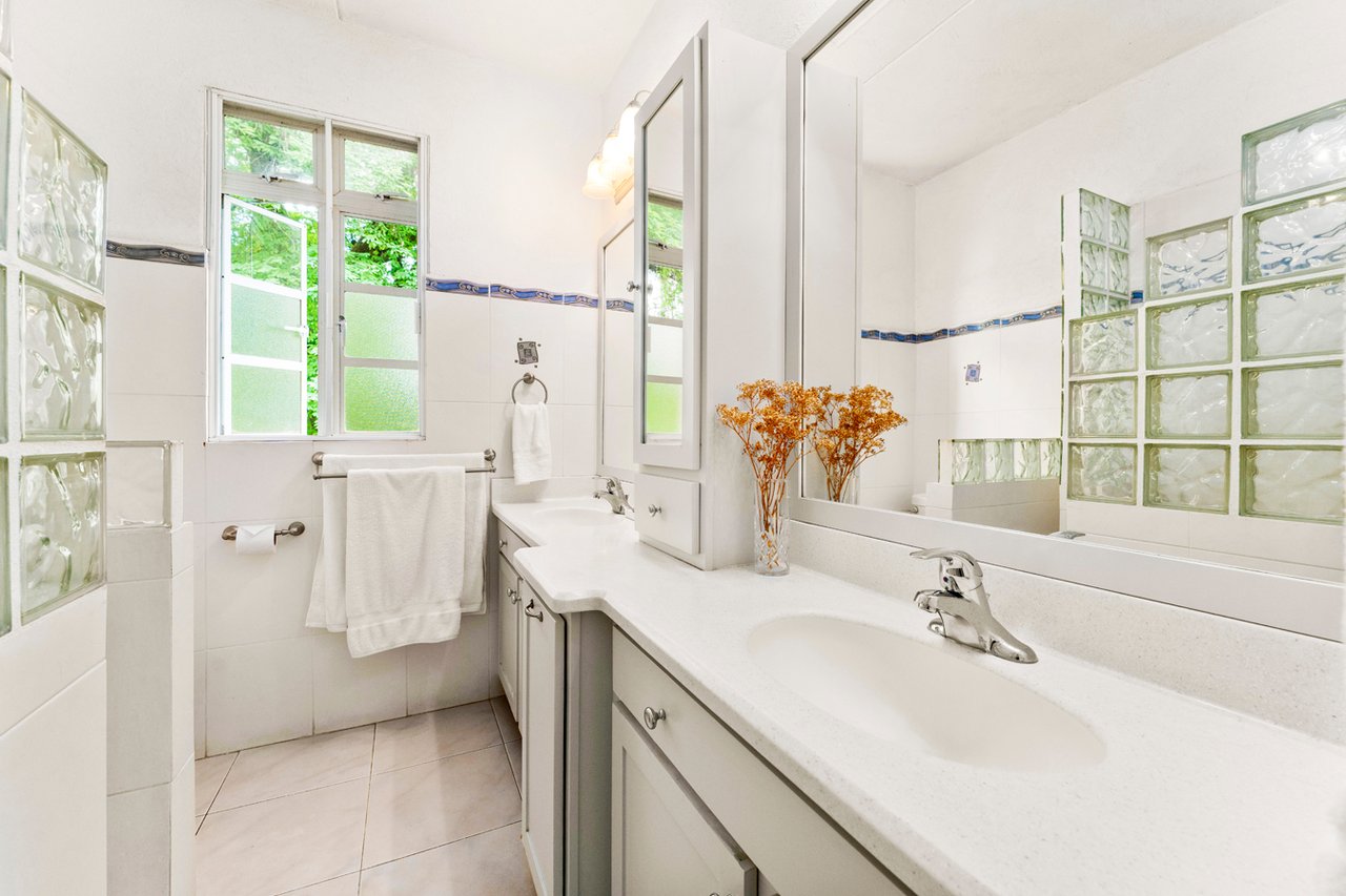 Bright bathroom with a long white vanity, large mirror, and translucent glass-block windows.