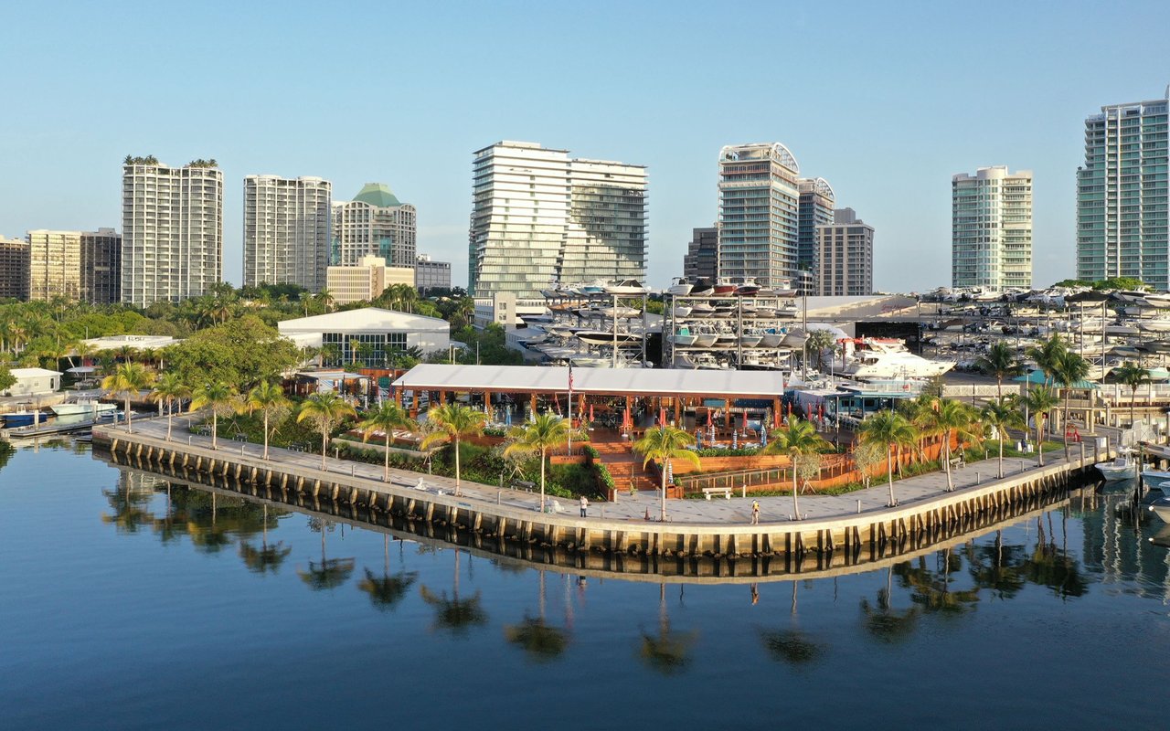 Coconut Grove waterfront marina with boats, palm-lined promenade, and high-rise buildings.