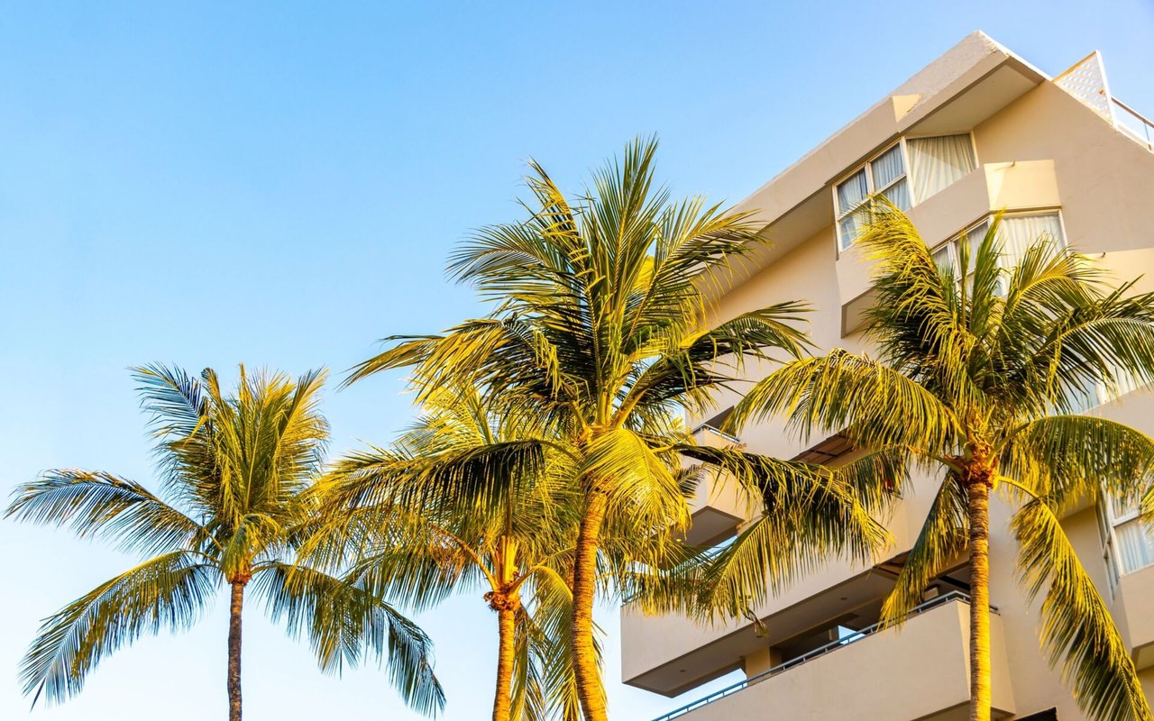 Tan condominium building with projecting balconies and tall palm trees.