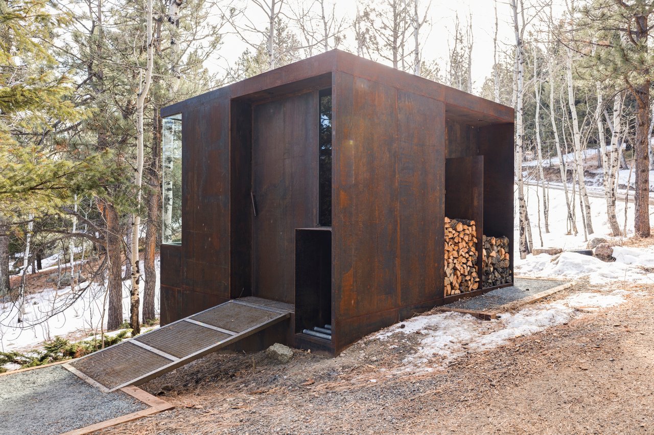 Modern steel storage shed with wood storage and ramp access, nestled among pine and aspen trees