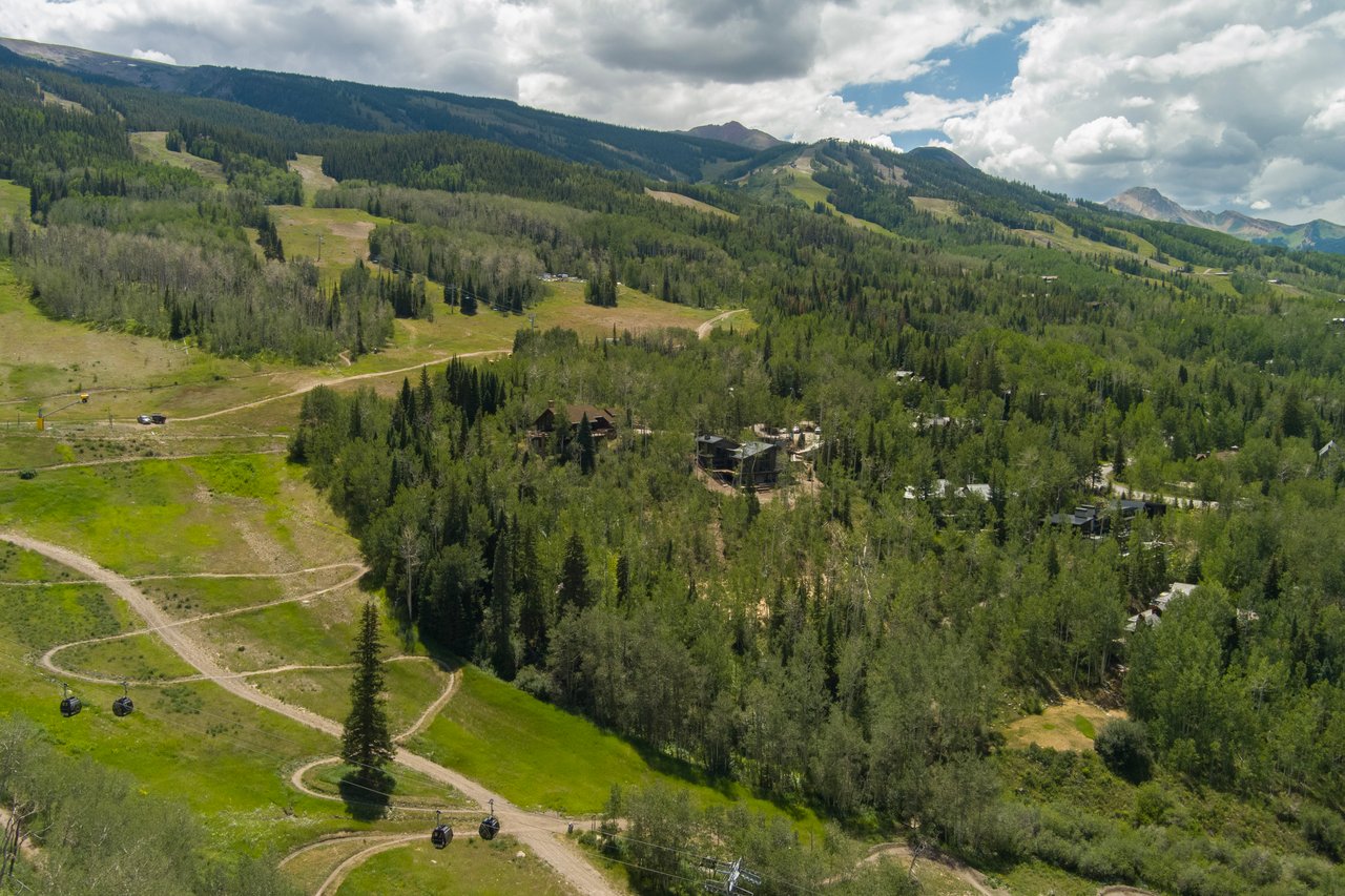 Aerial view of Snowmass mountain slopes, with gondola cabins crossing green trails and homes among the trees.