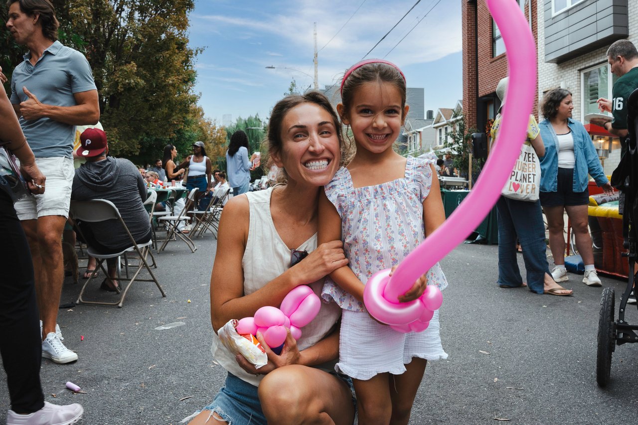 A woman and girl pose with pink balloon art at a neighborhood block party.