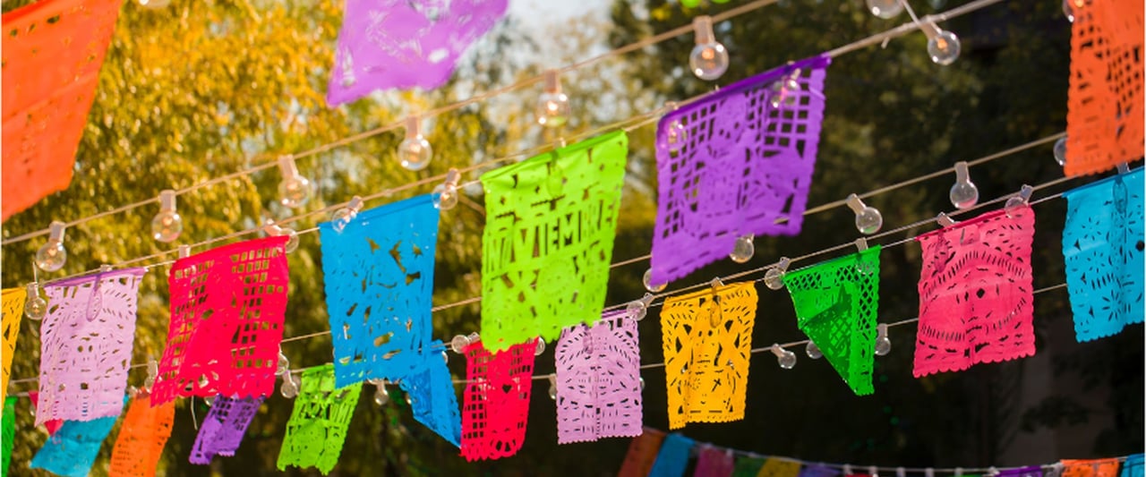 Colorful papel picado banners and string lights hanging outdoors for a Day of the Dead celebration.