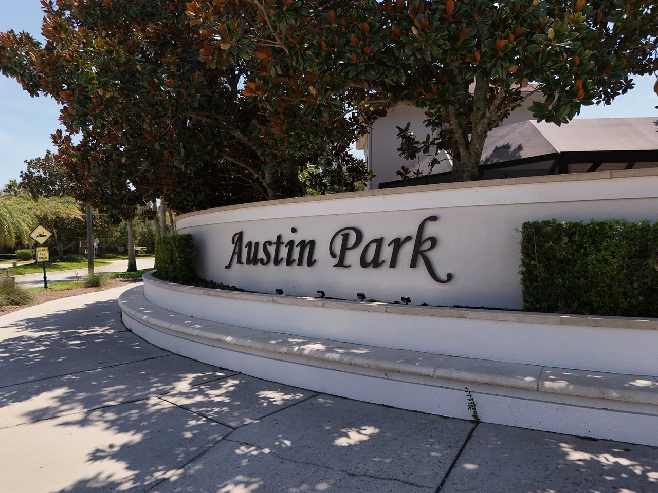 Austin Park neighborhood entrance sign beneath mature trees beside a sidewalk and road.