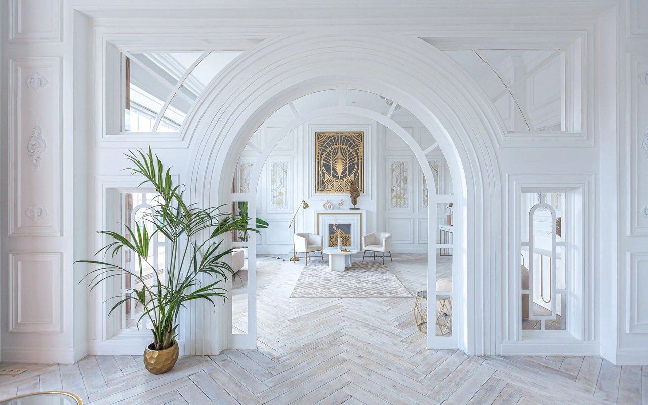 Ornate white living room with layered arches, gold accents, and a potted plant.