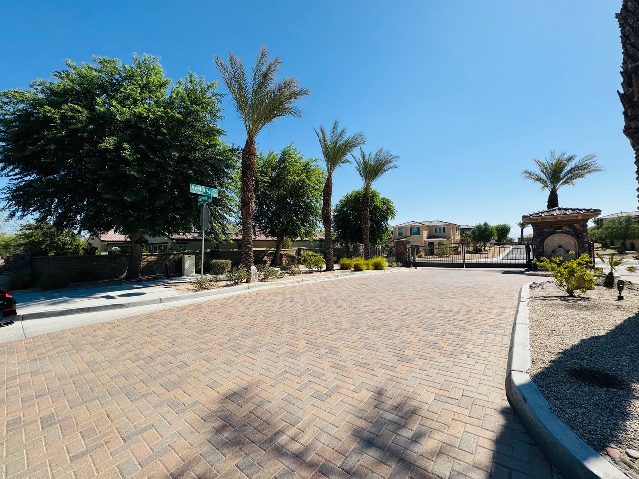 Avellana community entrance with a gated brick-paver drive, stone monument, and palm trees.