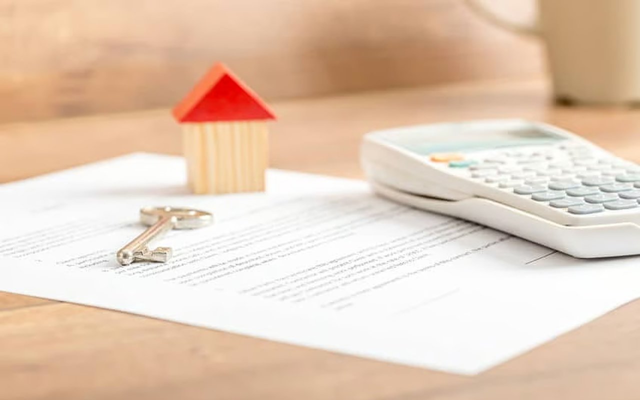 Small house model and key on mortgage paperwork beside a calculator.