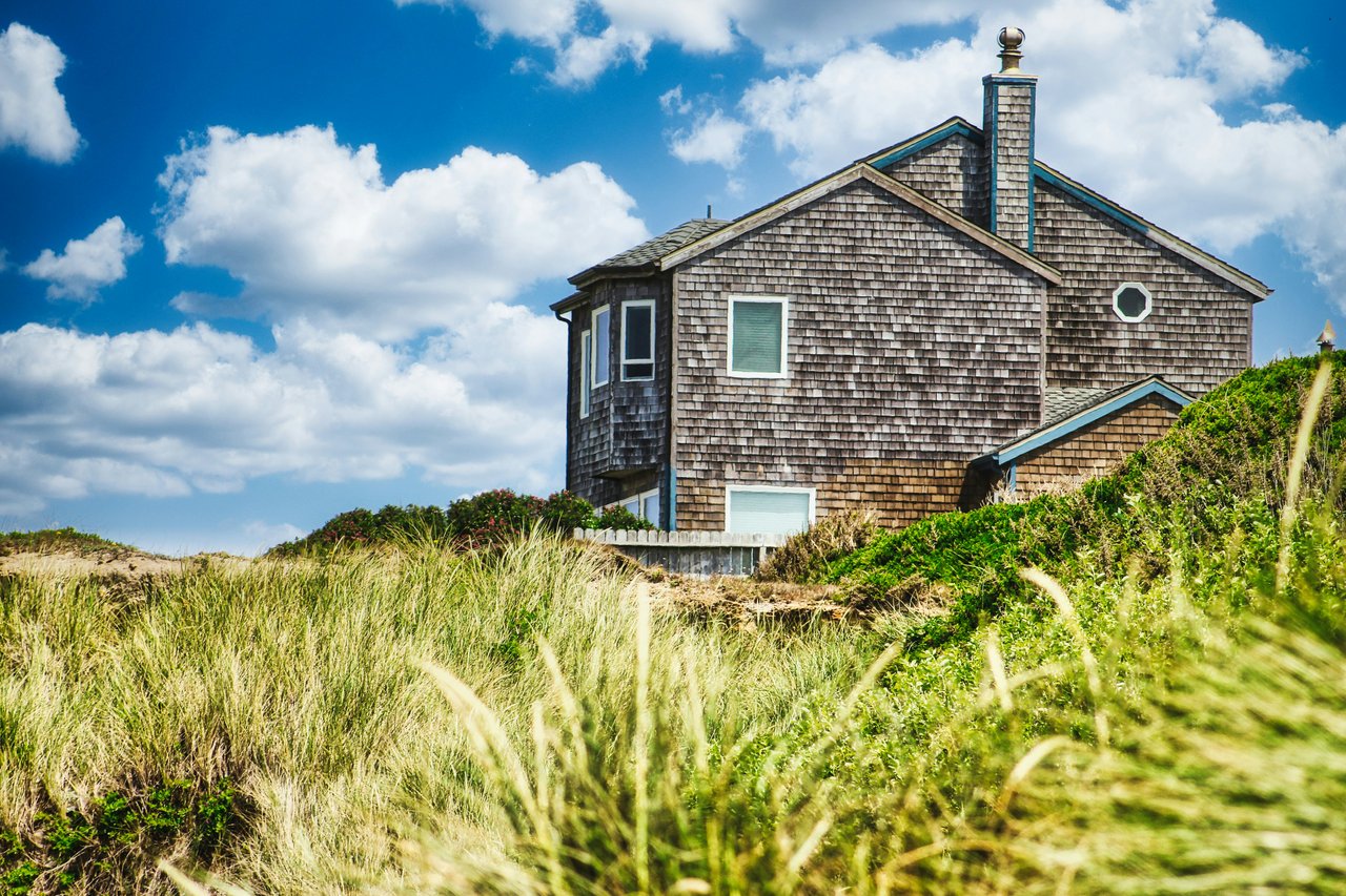 Shingle-sided house among dune grasses, with a steep gabled roof and octagonal window.