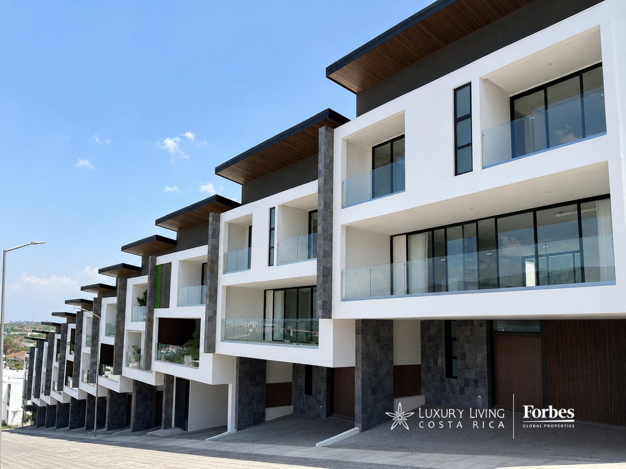 Contemporary white residential building with glass balconies, dark stone columns, and projecting wood-lined roofs.