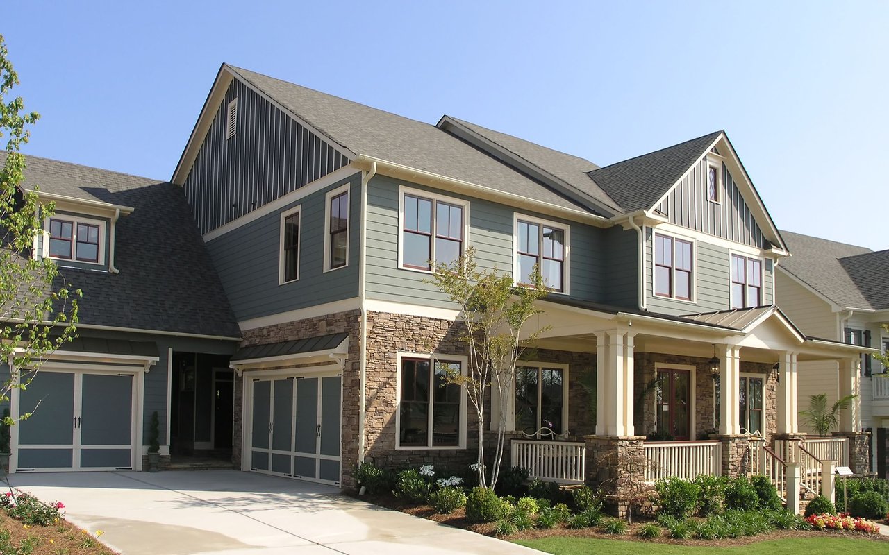 Two-story gray-green house with stone accents, multiple gables, a covered porch, and attached garages.