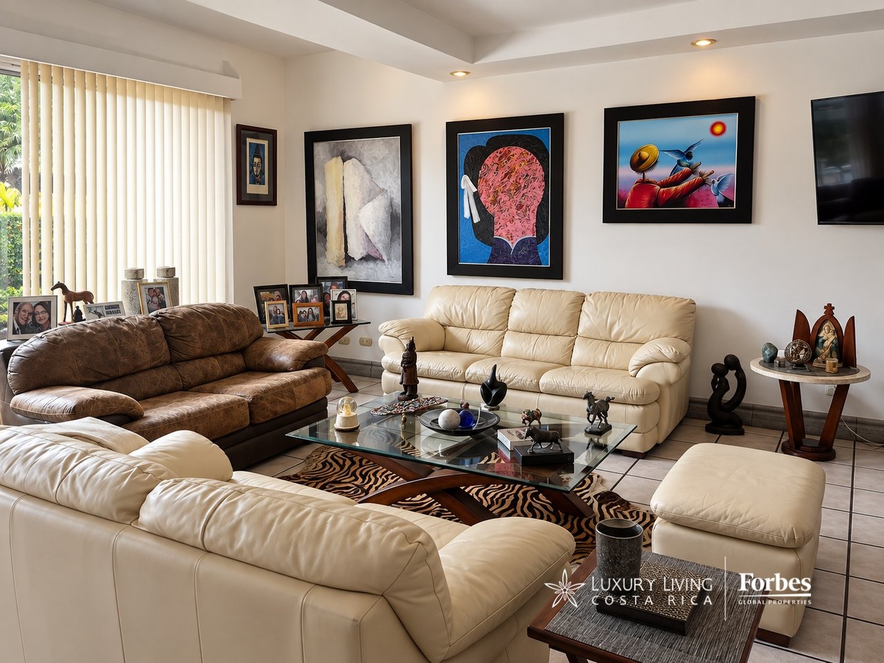 Furnished living room with cream leather sofas, a brown sofa, glass coffee table, and framed artwork.