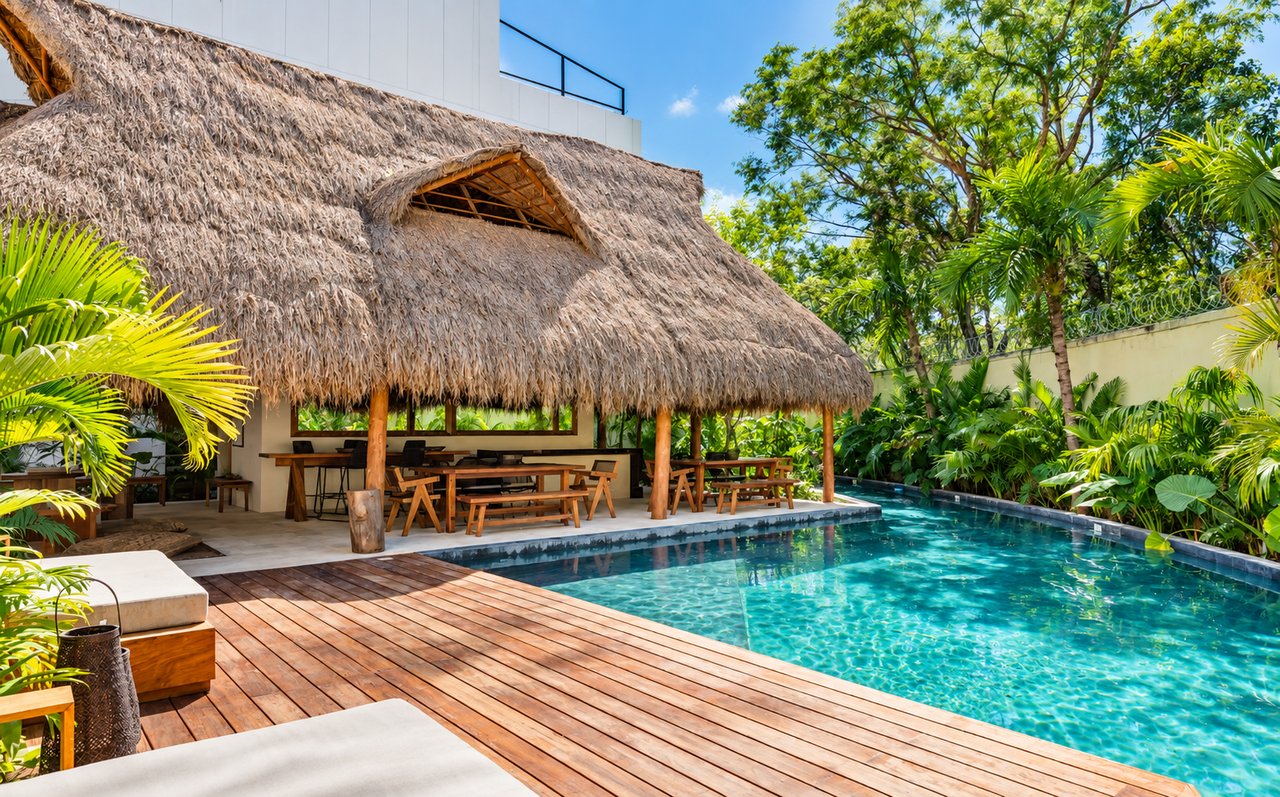 Pool and wooden deck beside a thatched-roof palapa surrounded by tropical greenery.