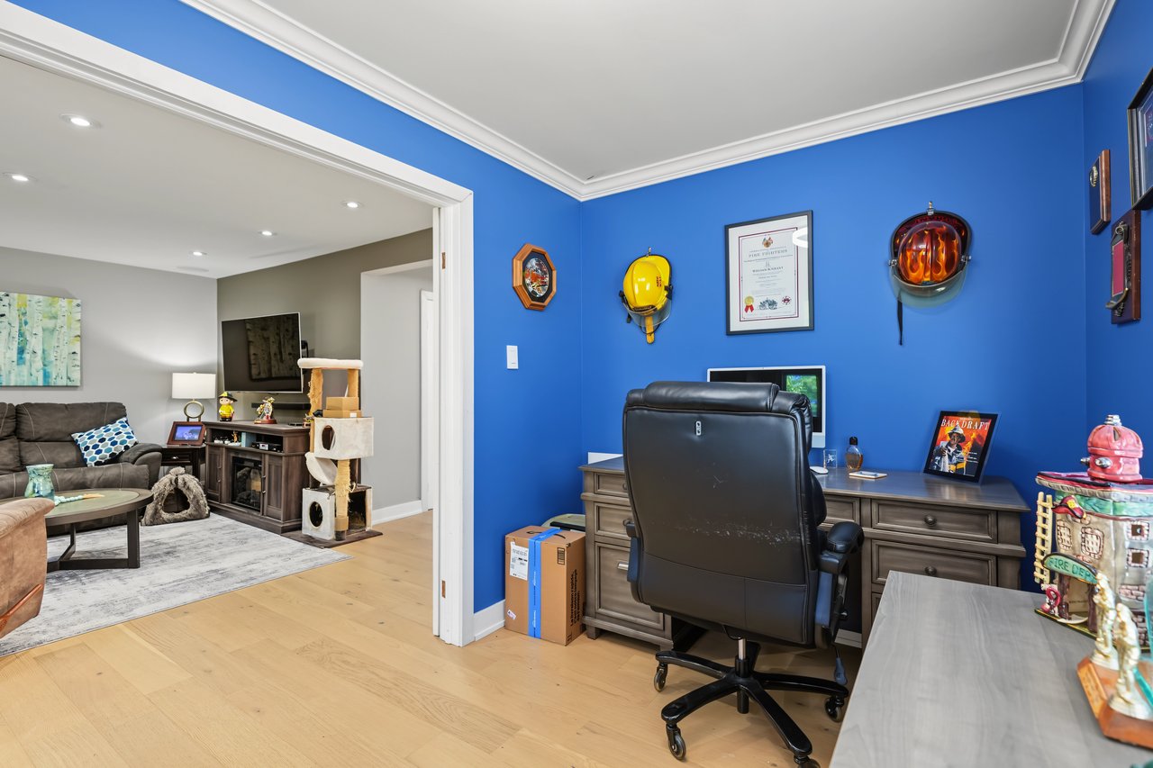 Furnished home office with blue walls and desk, opening into a living room with a sofa and cat tree.