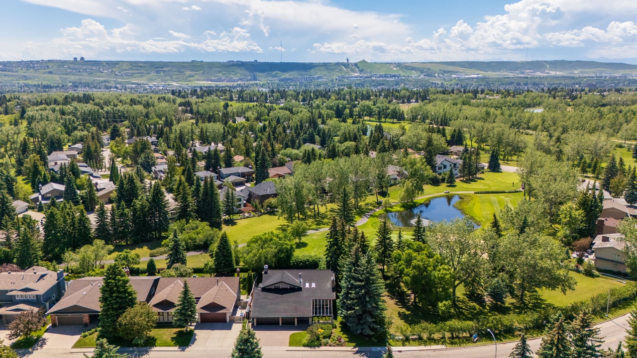 Aerial view of a Calgary home beside a tree-lined park and pond.