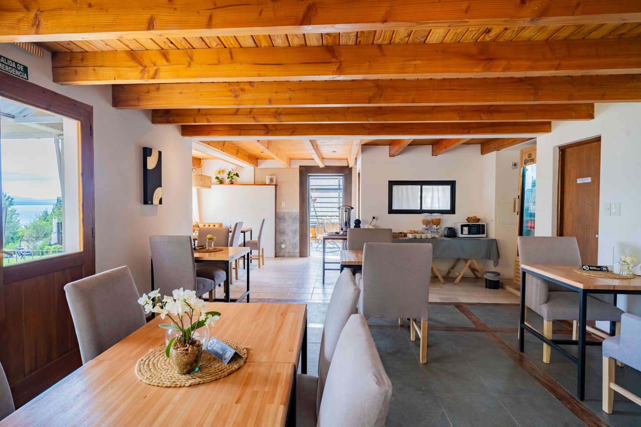 Hotel dining lounge with timber ceiling beams, wooden tables, and water visible through the window.