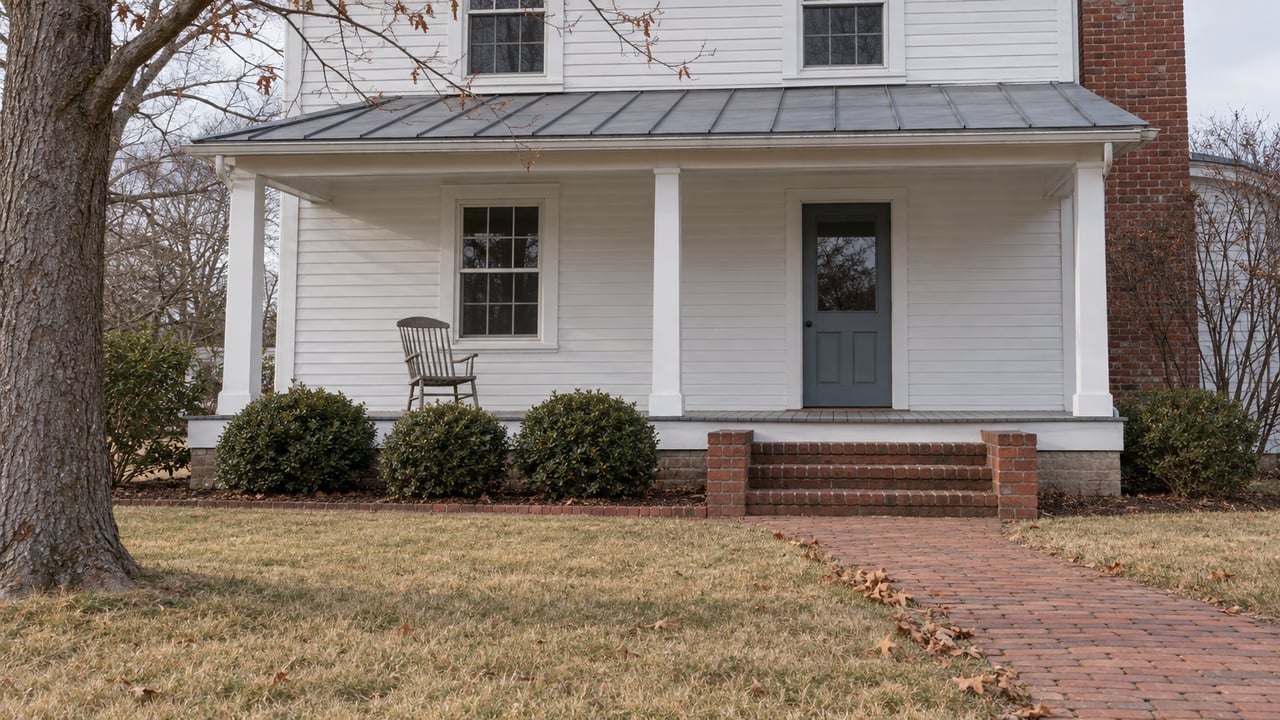 White clapboard home with a blue-gray entry door, covered porch, brick steps and a curving walk through a dormant winter lawn.