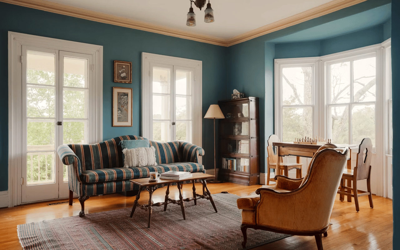 Teal living room with a striped sofa, tall windows, hardwood floors, and a chess table.