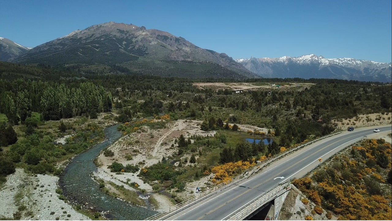 Aerial view of a river valley with a highway bridge and mountain range beyond.