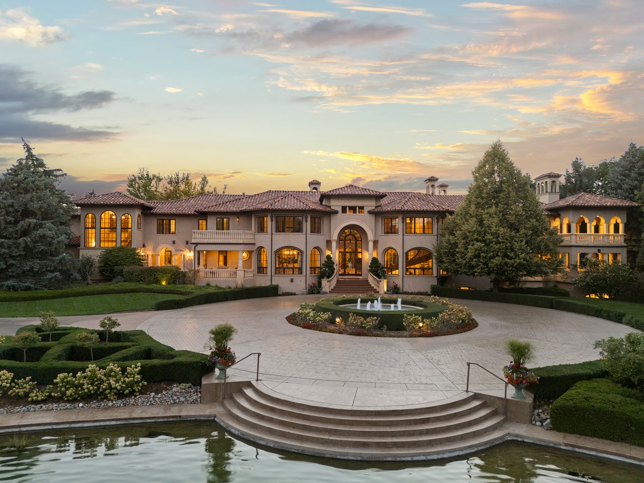 Mediterranean-style estate with a fountain courtyard, formal gardens, and reflecting pool at sunset.