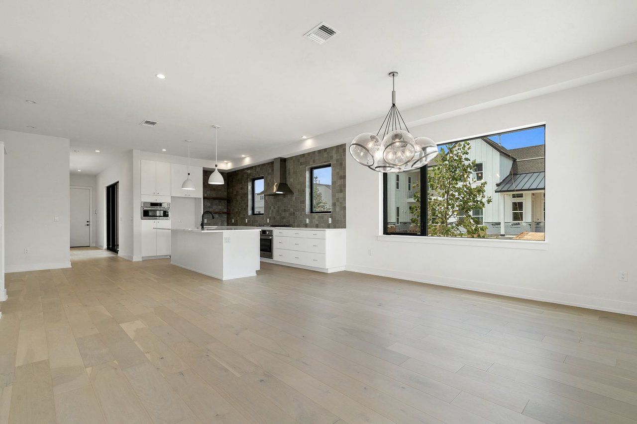 Open-plan kitchen with a white island, dark tiled backsplash, pale wood floors, and glass globe chandelier.