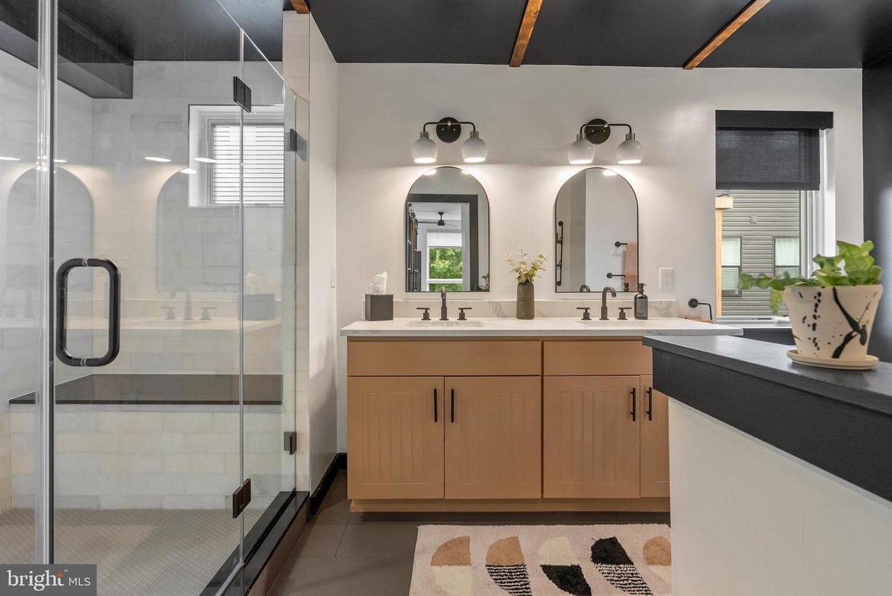 Modern bathroom with a glass shower, double vanity, arched mirrors, and warm wood cabinetry.