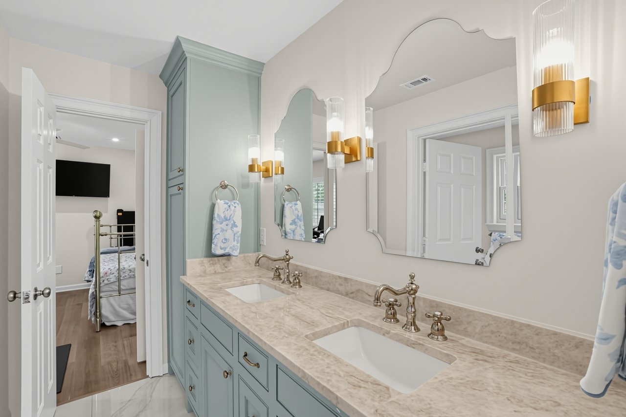 Bathroom with a pale blue double vanity, marble-look counter, ornate mirrors, and gold-and-glass sconces.