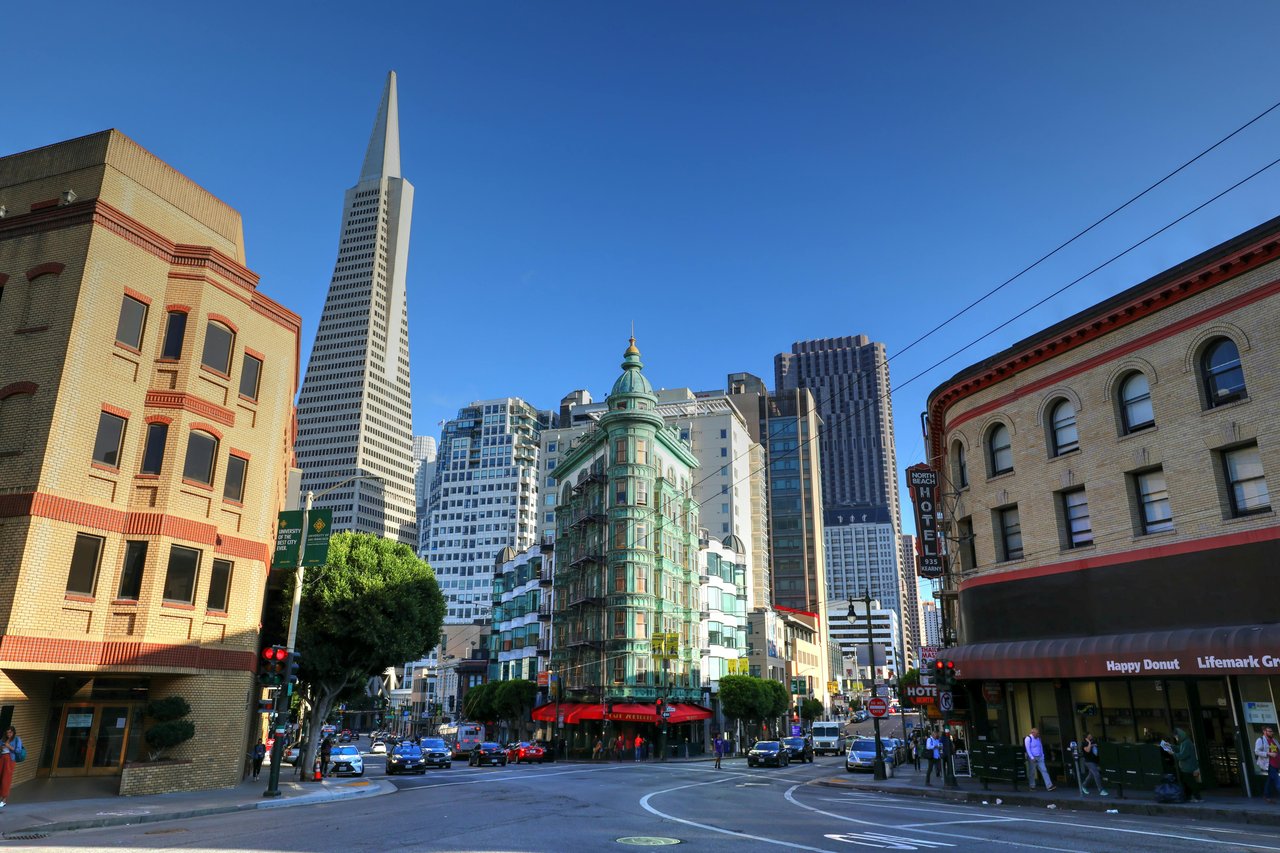 Iconic view of North Beach in San Francisco featuring the historic Sentinel Building with its green facade, the Transamerica Pyramid in the background, and a vibrant street scene with classic architecture and city traffic.