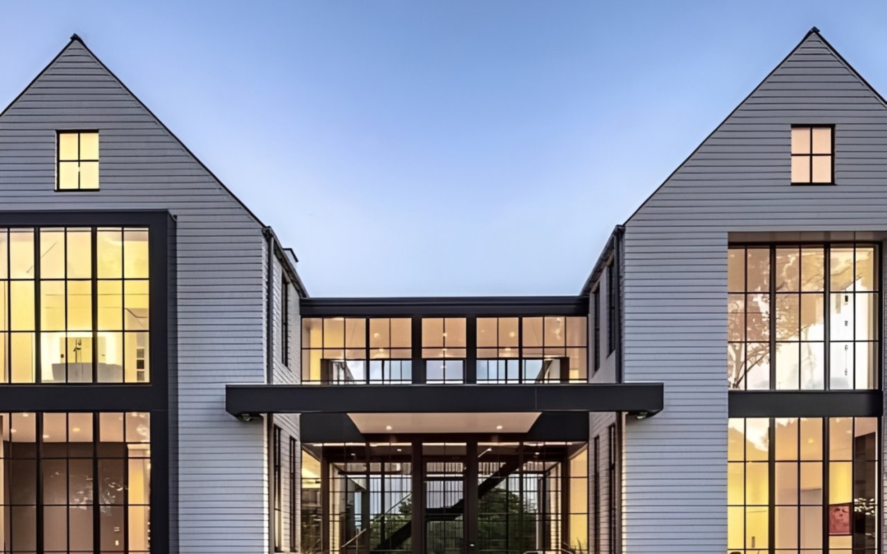 Modern gray house with steep gables and broad illuminated windows at dusk.