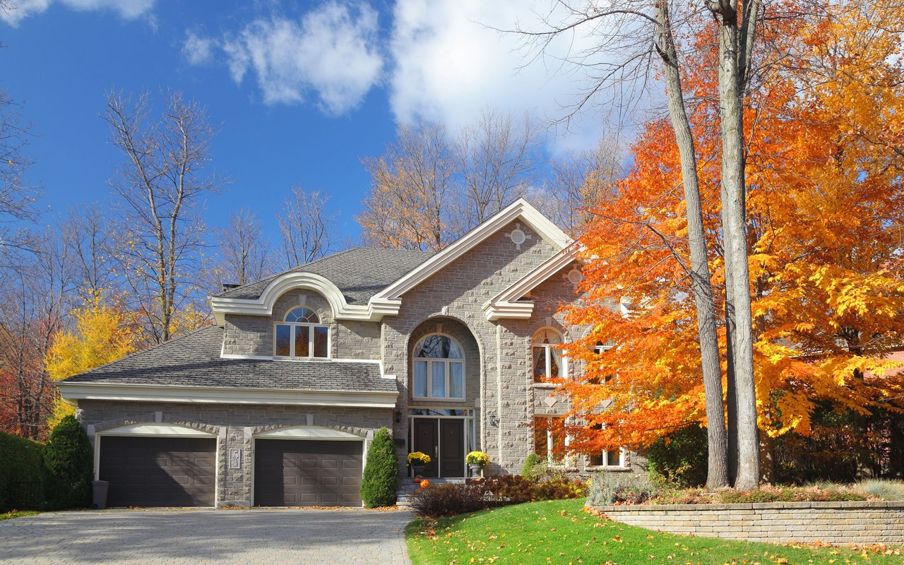 Stone-fronted two-story home with arched windows, a double garage, and autumn trees.