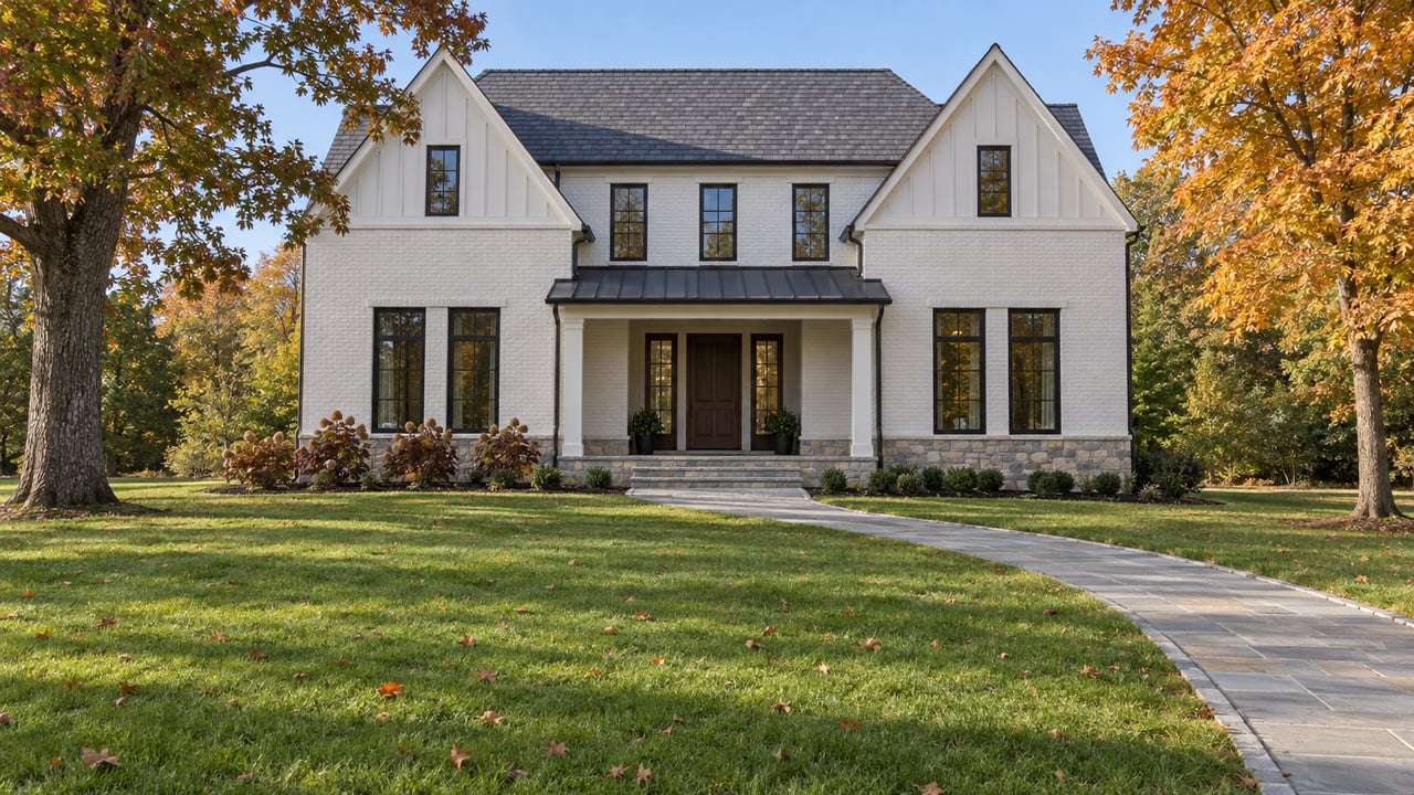 White brick gabled home beyond a broad autumn lawn, framed by an oak and an amber maple.