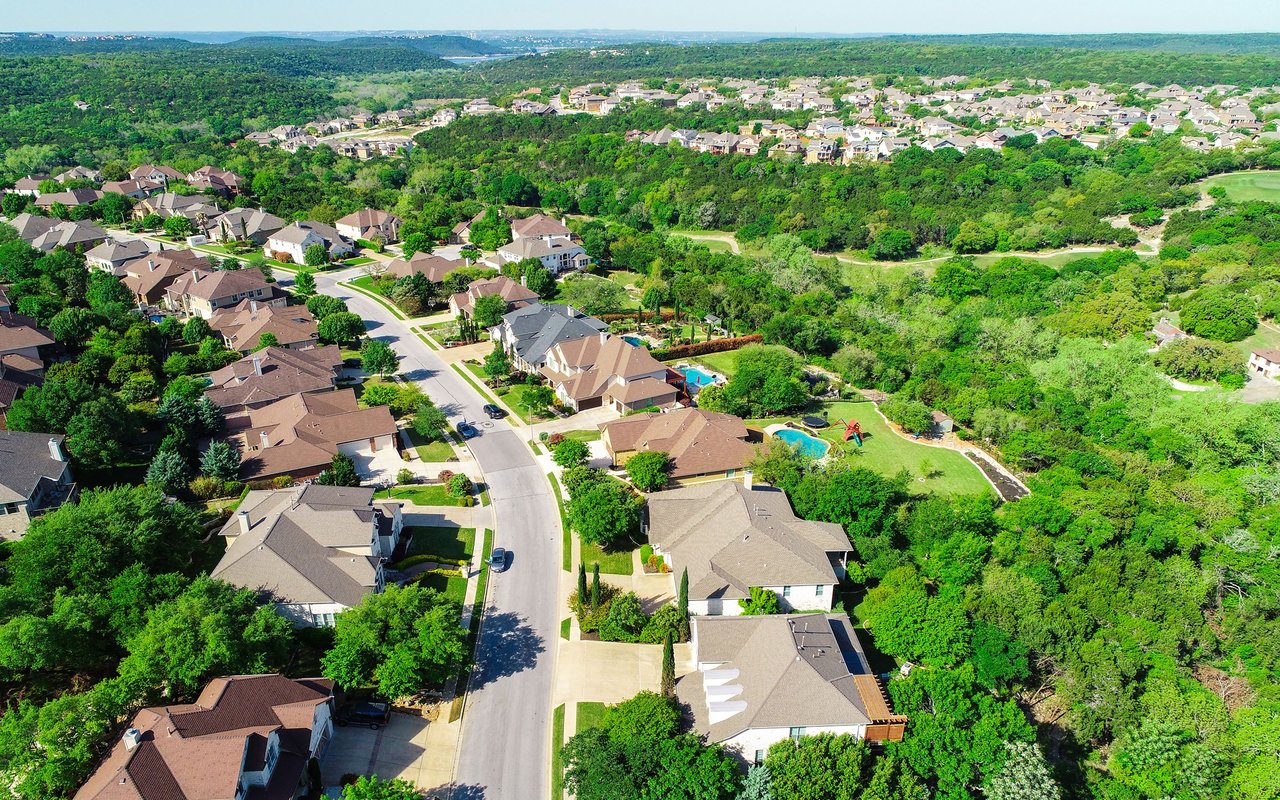 Aerial view of a leafy neighborhood with winding streets, detached homes, and backyard pools.