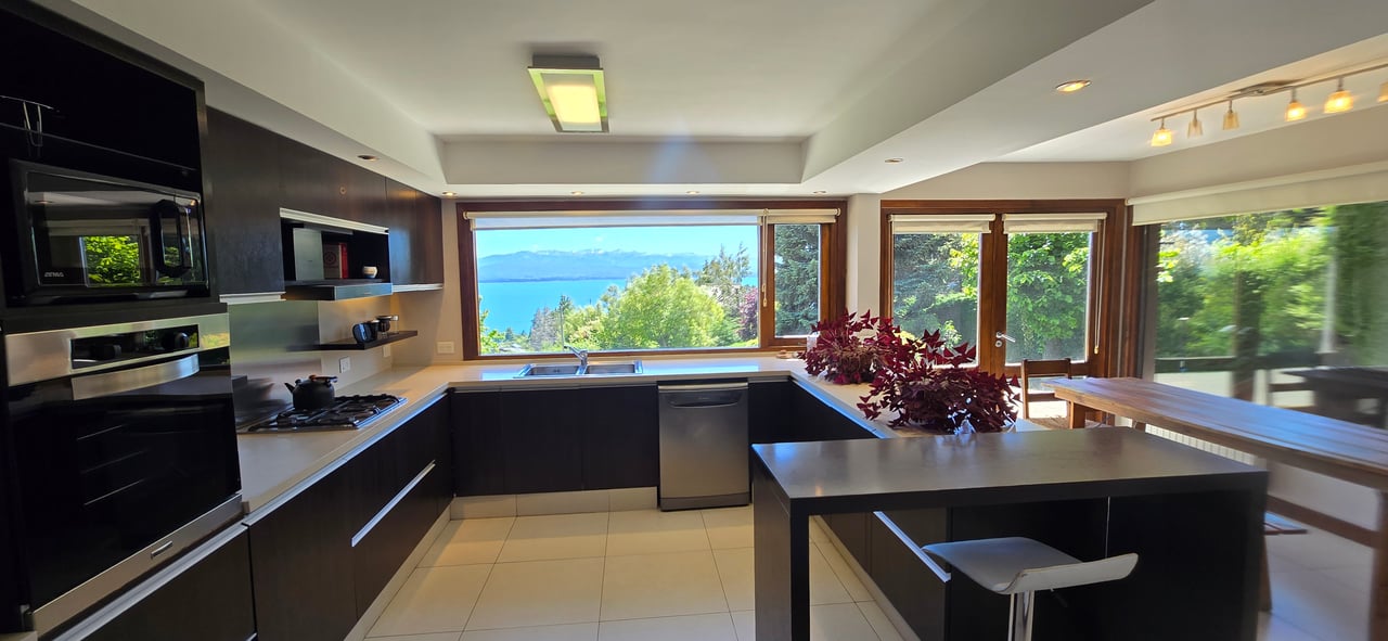 Modern kitchen with a large island and windows overlooking a lake and distant mountains.