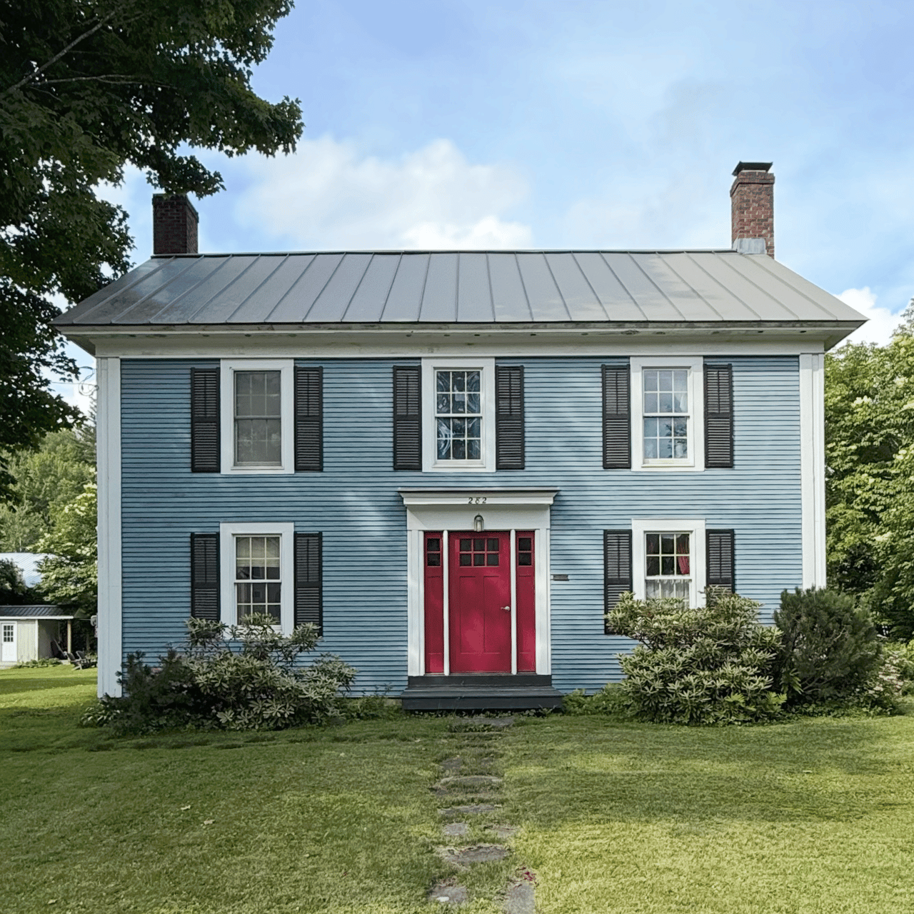 Blue two-story house with a red front door, black shutters, and a gray metal roof.