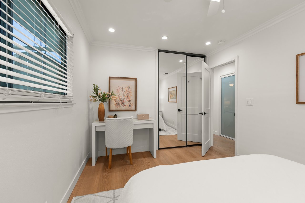 Bedroom with mirrored closet doors and a desk beneath floral artwork.