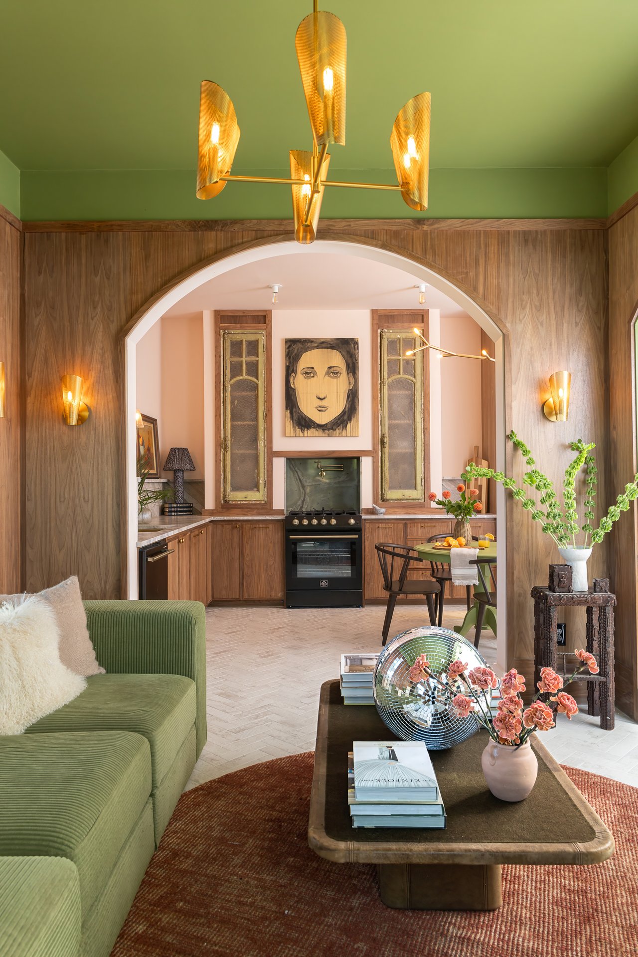 Open-plan living room and kitchen with green sofa, wood paneling, and an arched opening.