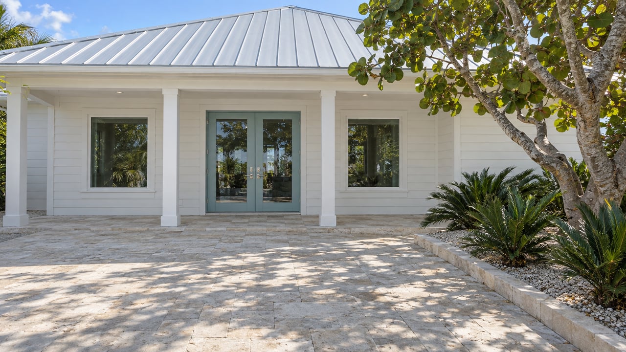 White coastal cottage with a silver metal roof, sea-glass blue double doors and a limestone courtyard shaded by a sea grape tree.