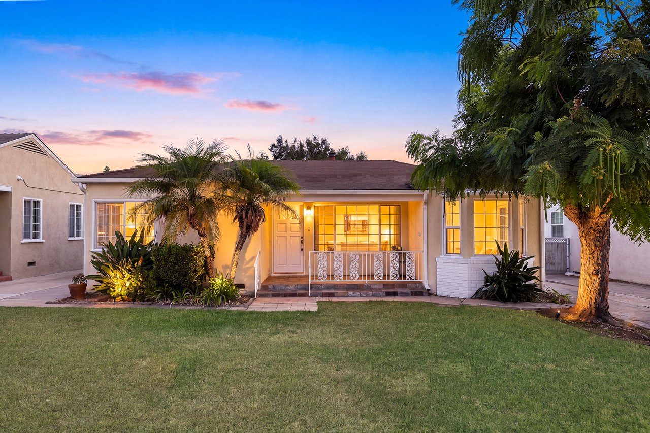 Single-story home with a covered porch, palm trees, and a broad lawn at dusk.
