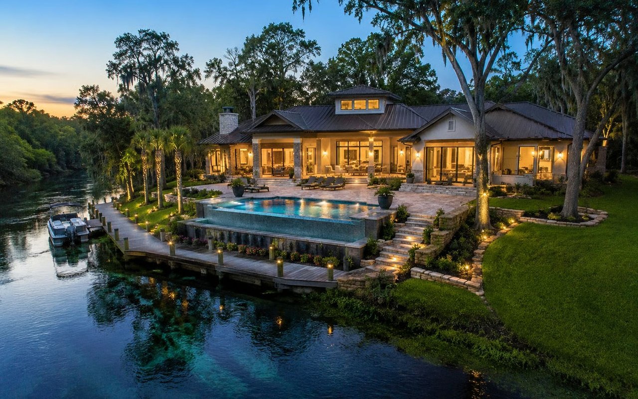 Waterfront home with an infinity pool and dock beside a river at dusk