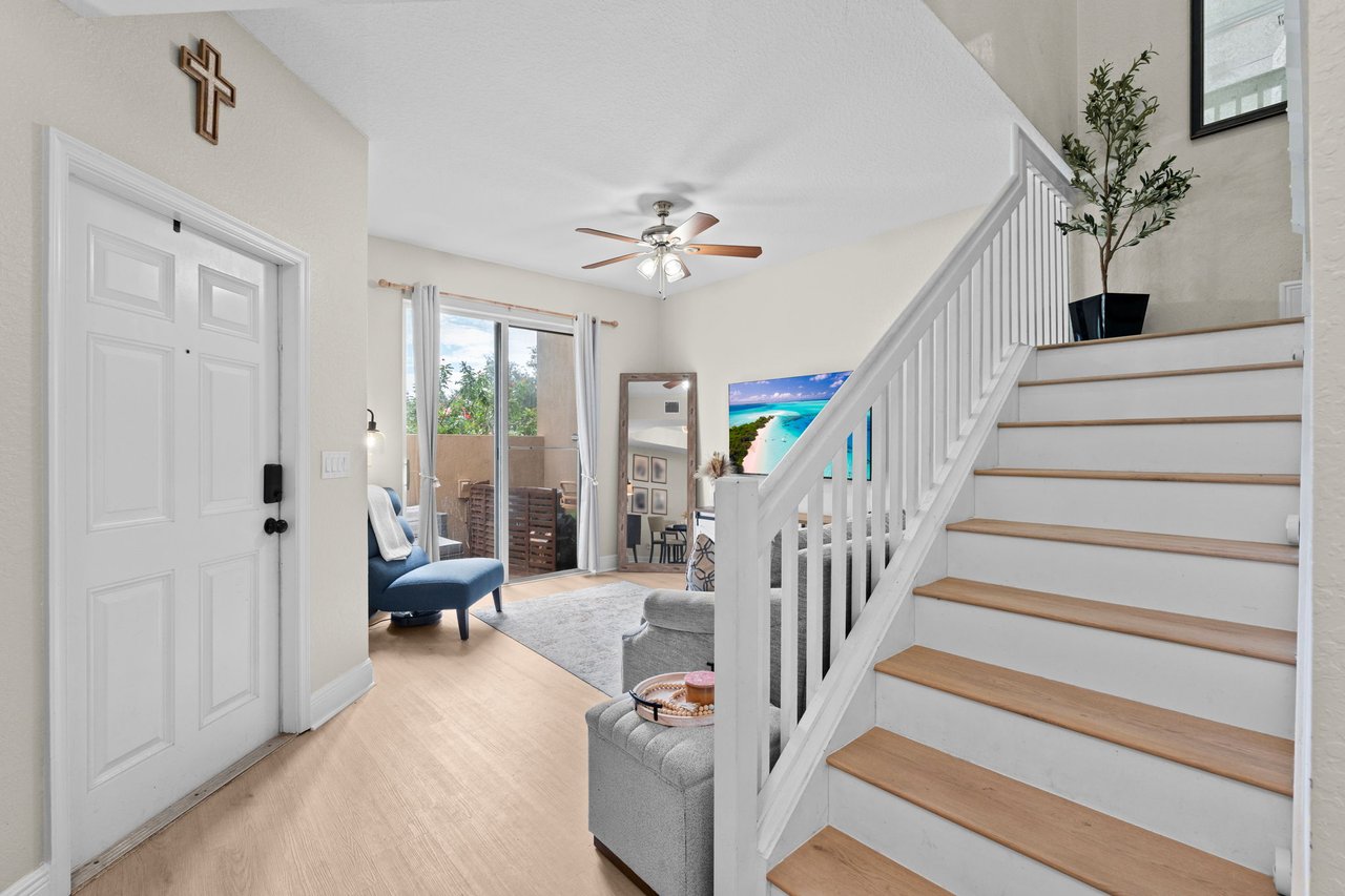 Bright entryway and living area with a white staircase, wood treads, and sliding doors to a patio.