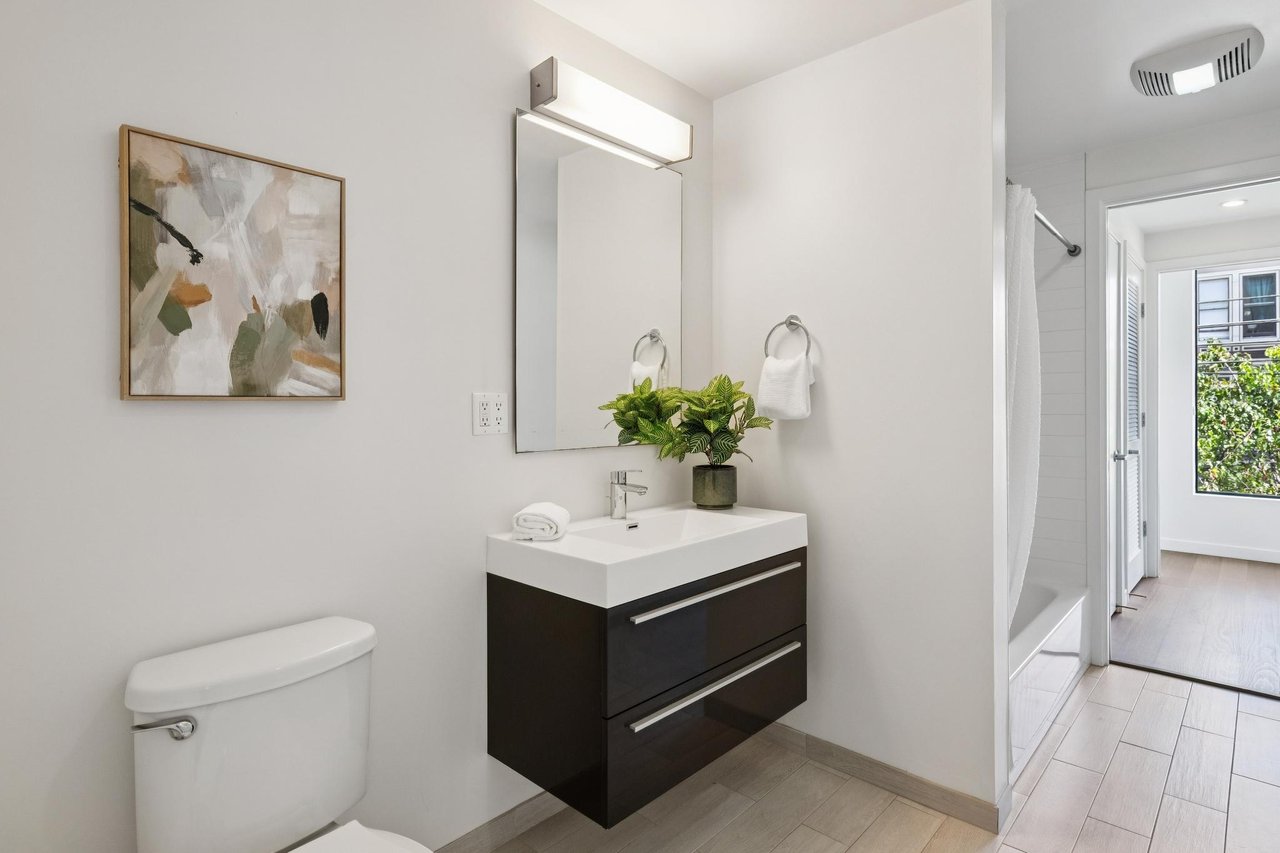 Bright bathroom with a dark floating vanity, large mirror, and partially visible tub and shower.